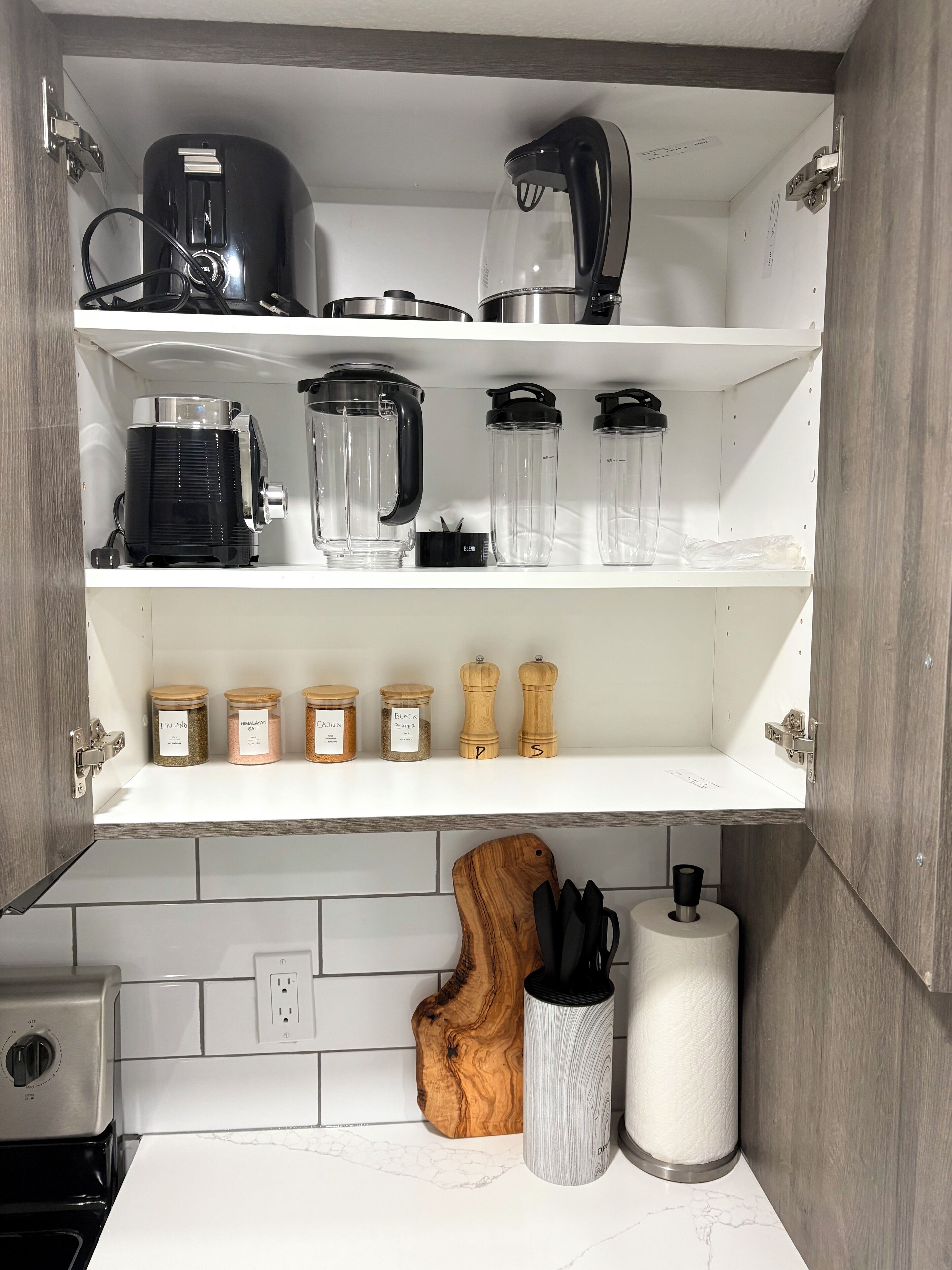 A kitchen with a built-in coffee maker, a blender, and spice jars on the upper shelf.
