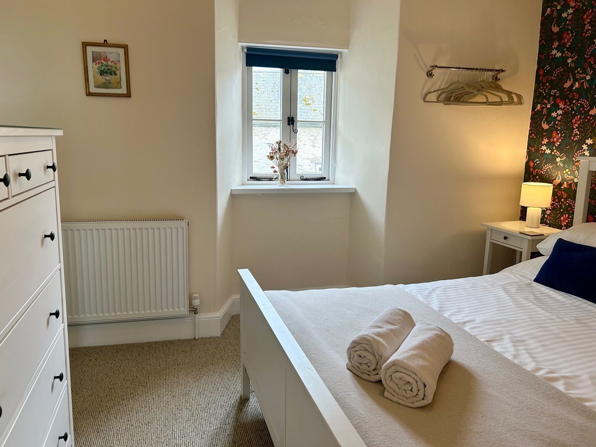 Een slaapkamer met een bed, een kaptafel, een radiator, een raam en een nachtkastje met een lamp.