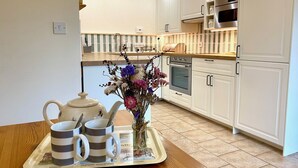 Une cuisine moderne avec des meubles blancs, un four en acier inoxydable et un grille-pain. Un plateau avec des tasses et une théière est posé sur la table en bois.