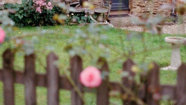 Une maison en pierre avec une roue en bois, une fenêtre ornée d’un rideau et une porte avec une plaque nominative.