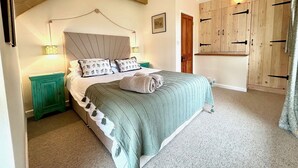 Une chambre à coucher comprenant un lit, une table de chevet, une armoire en bois et un plafond avec des poutres apparentes.