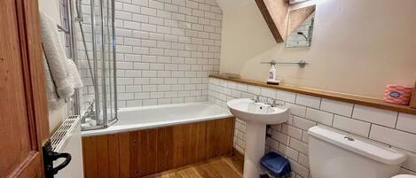 A bathroom with a shower, sink, toilet, and wooden flooring.