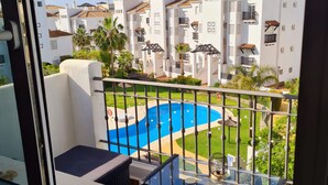 A balcony with a glass table, a view of a swimming pool, and white buildings in the background. - 🌴 **Luxury Coastal Getaway – 2 Bed, 2 Bath Apartment with Pool Views** 🌴
 (Manilva)