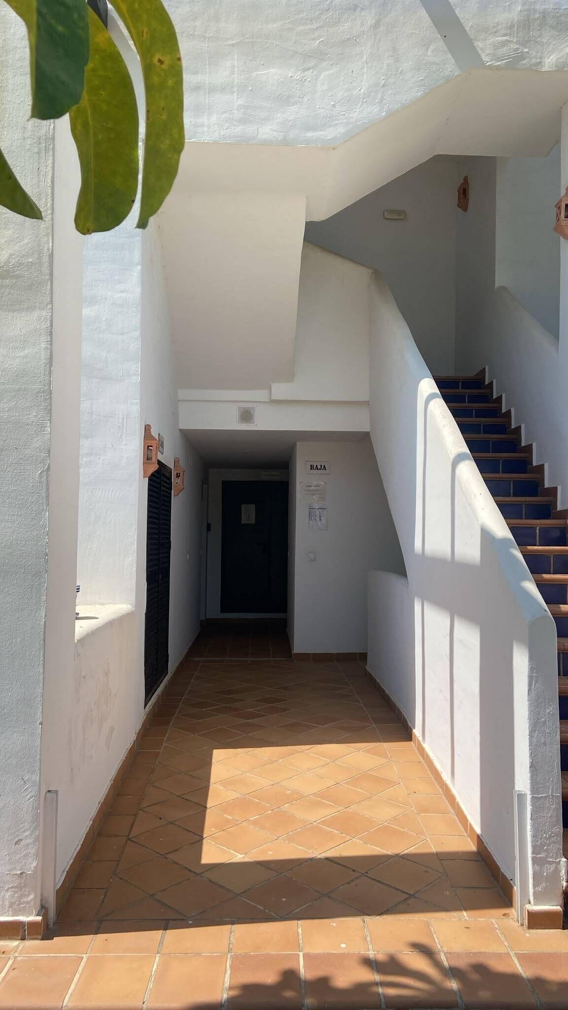 Um corredor com chão de azulejos, uma escadaria à direita e uma porta no final.