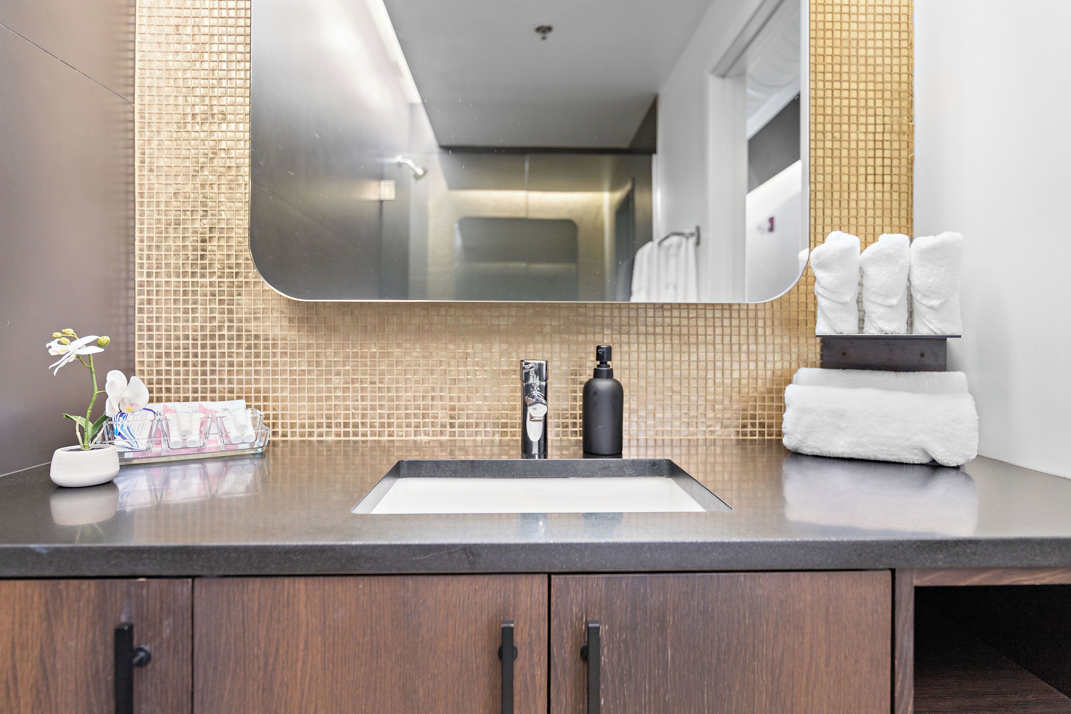 Une salle de bain avec un plan de toilette foncé, un lavabo, un miroir et un porte-serviettes.