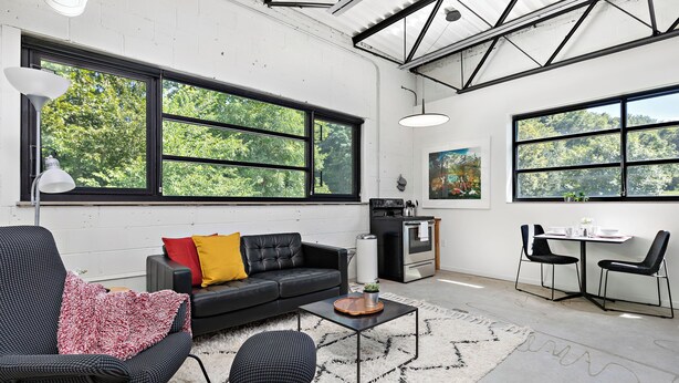 A modern living room with large windows, a sofa, a coffee table, and a dining area.