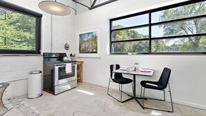 A modern kitchen with a large window, a dining area with two chairs, and a painting on the wall.
