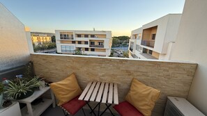 A balcony with a table and chairs, a potted plant, and a view of neighboring buildings.