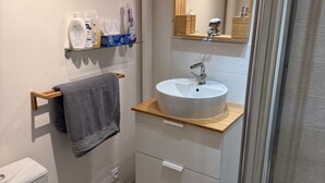 A modern bathroom with a white sink, wooden countertop, and a mirror above it. There is a towel hanging on a rack, a toilet, and a shower area with a glass door.