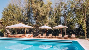 Une piscine entourée d’arbres, avec des chaises longues et des parasols.