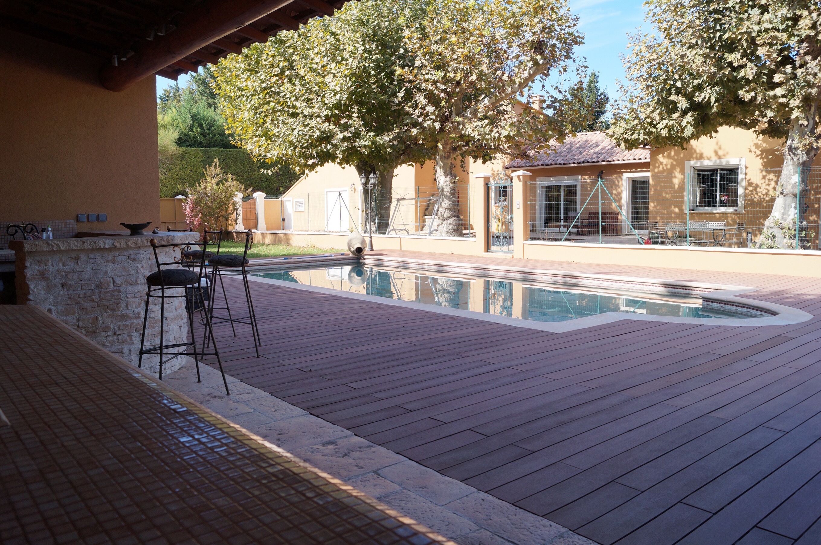 An outdoor pool area with a wooden deck, two bar stools, and a stone wall.