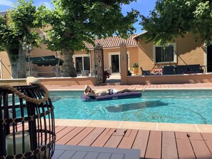 A pool area with a floating lounge chair, a rope barrier, and a view of a building with a tiled roof and windows. - Large detached villa in Avignon for 12 people (Avignon)