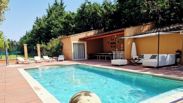 Una piscina con cubierta de madera, sillas de descanso, un sofá y un área de patio techada.