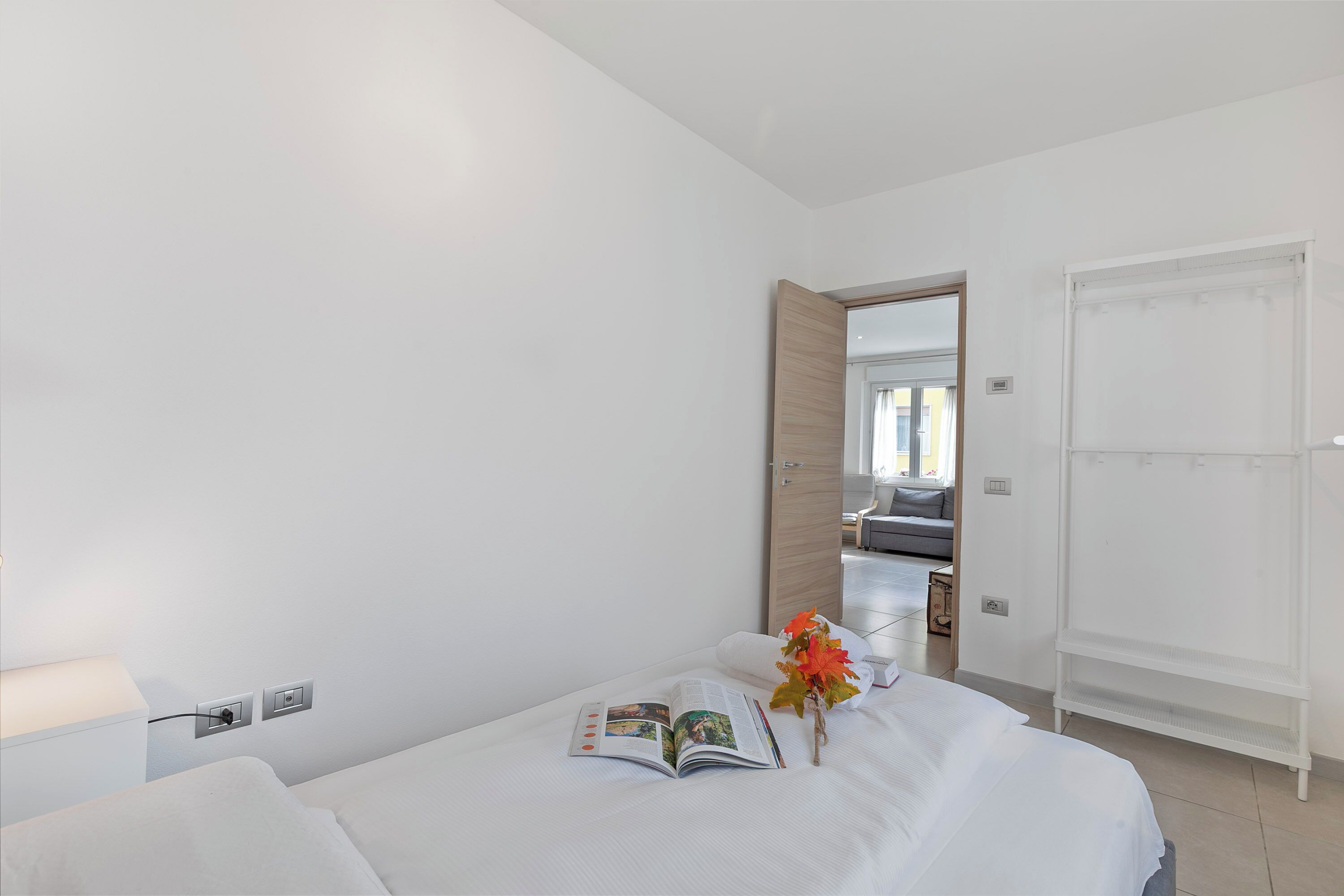A hotel room with a bed, a nightstand, a lamp, a mirror, and a door leading to another room.