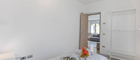 A hotel room with a bed, a nightstand, a lamp, a mirror, and a door leading to another room.