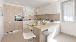 A modern kitchen with a central island, white cabinetry, and a window with sheer curtains. - Thomas's House (Riva del Garda)