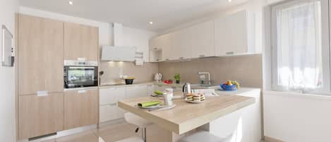 A modern kitchen with a central island, white cabinetry, and a window with sheer curtains.
