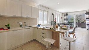 A modern kitchen with a central island, a dining area with a table and chairs, and a view of the outdoors through large windows. - Thomas's House (Riva del Garda)