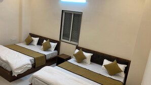 A hotel room with two single beds, each with a wooden headboard, white bedding, and brown decorative pillows. There is a small wooden nightstand between the beds, and a window with a metal screen above.