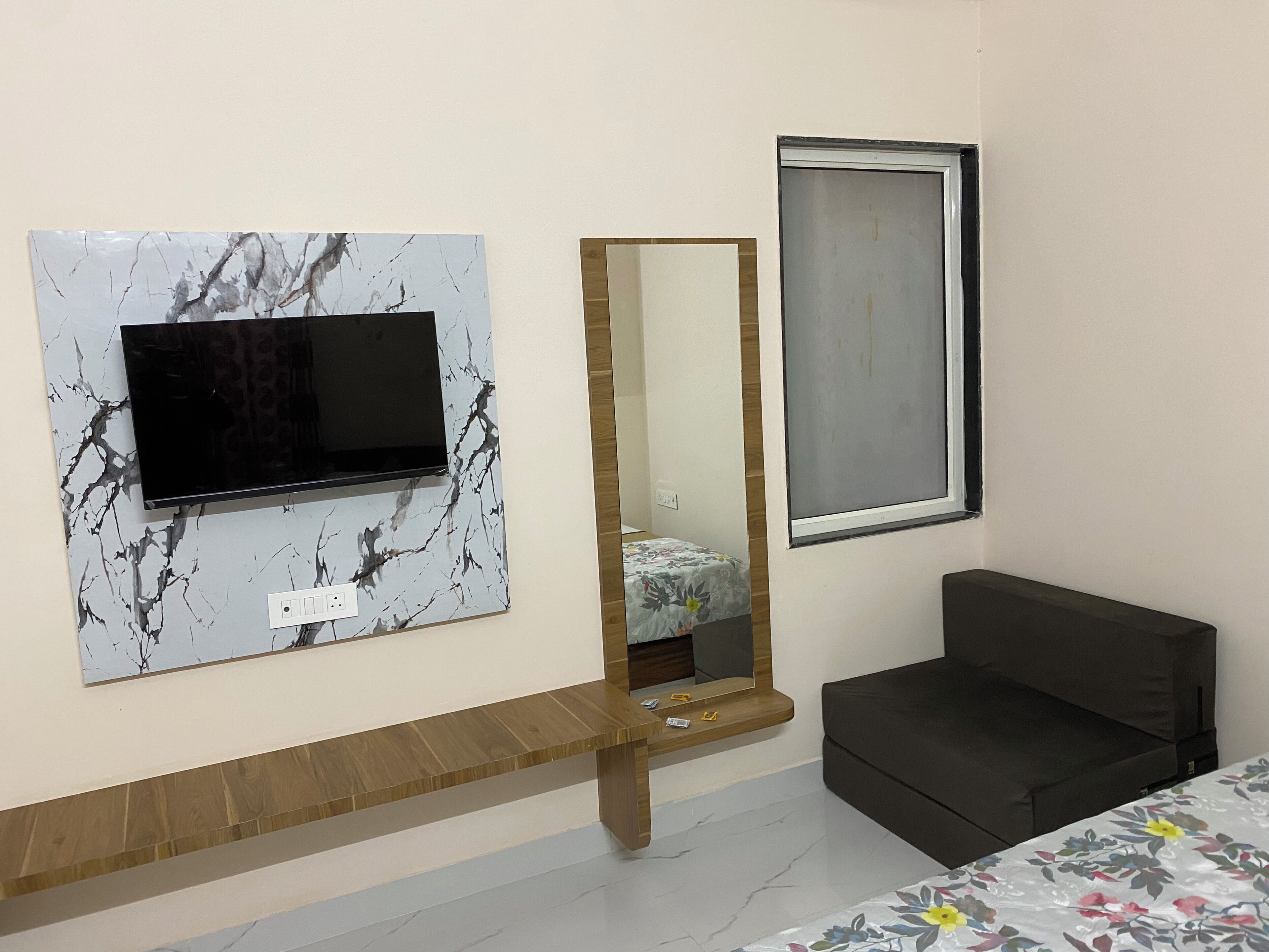 A room with a mounted TV, a mirror, a bed, and a window.
