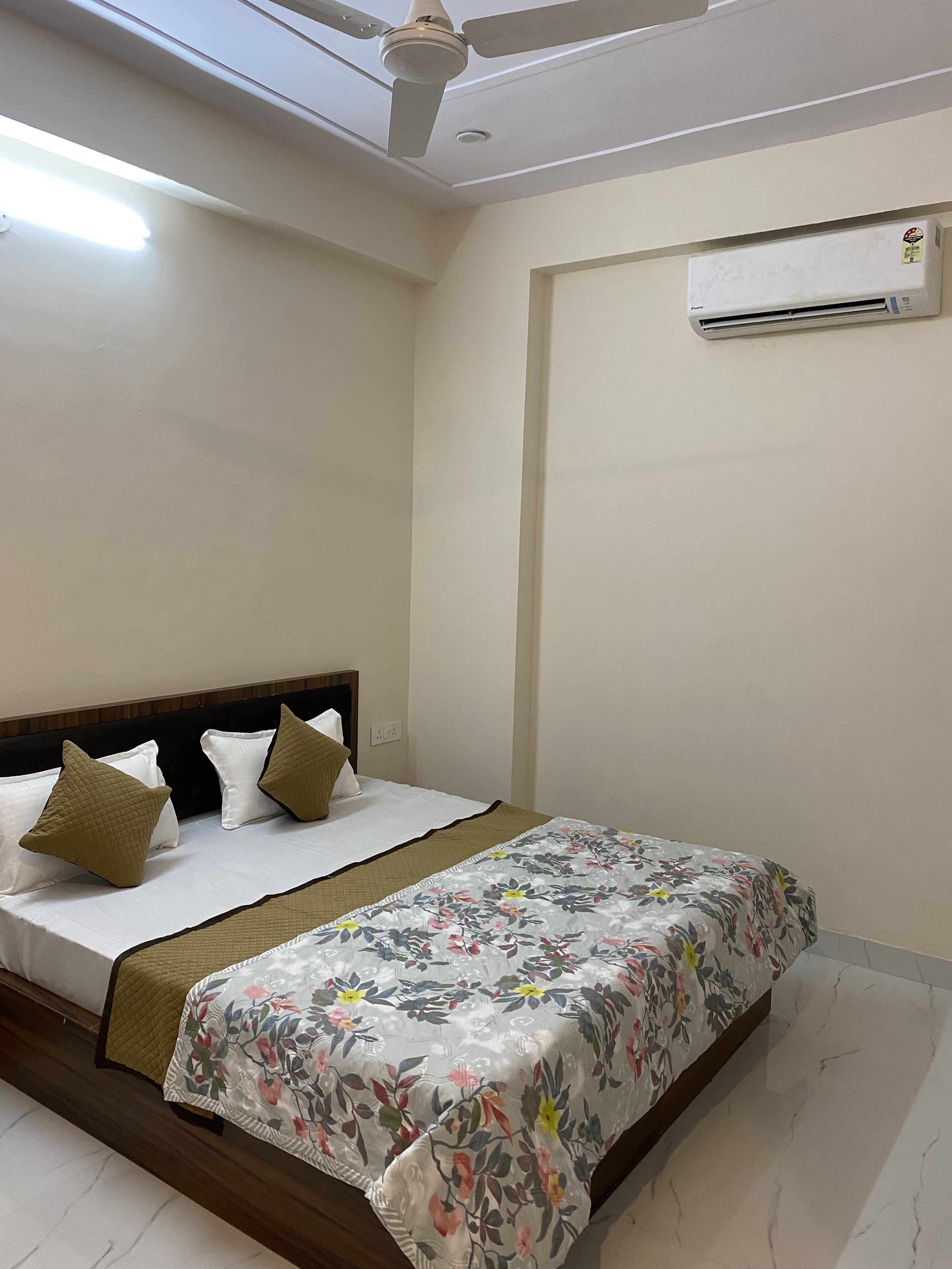 A bedroom with a bed, a ceiling fan, an air conditioning unit, and a floral bedspread.