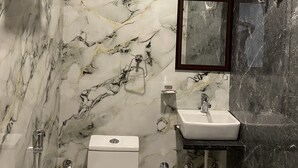 A bathroom with marble walls, a white sink, a toilet, and a shower.