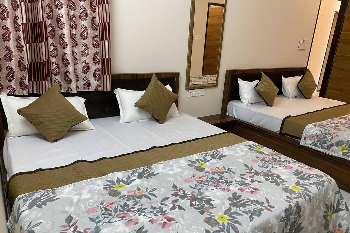 Ein Hotelzimmer mit zwei Betten, jedes mit weißer Bettdecke und braunen Kissen. An der Wand befindet sich ein Spiegel und ein gemustertes Vorhang.