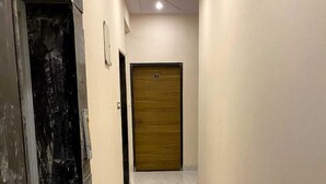 A corridor with a marble floor, a wooden door at the end, and a black door on the left.