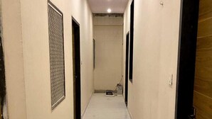 A hallway with white tiled floors and beige walls, featuring doors and a small area with a chair and a table.