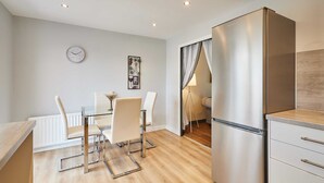 A modern kitchen with a stainless steel refrigerator, a dining table with chairs, a clock on the wall, and a floor lamp. - Host Stay Venture Park Villas (Kettering)