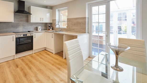 A modern kitchen with white cabinetry, a built-in oven, and a large window providing natural light. - Host Stay Venture Park Villas (Kettering)