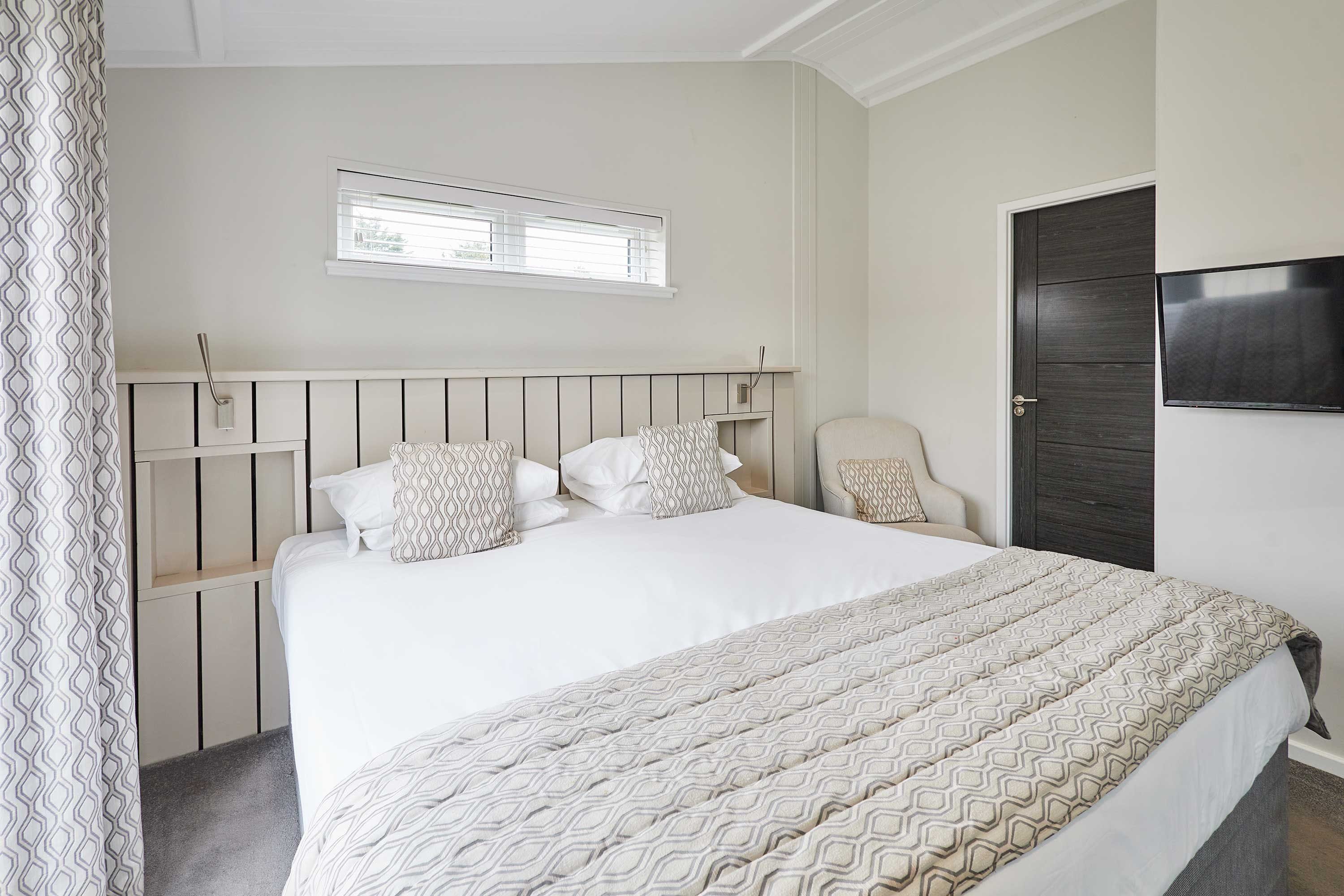 A neatly arranged bedroom with a bed, a television, and a window.