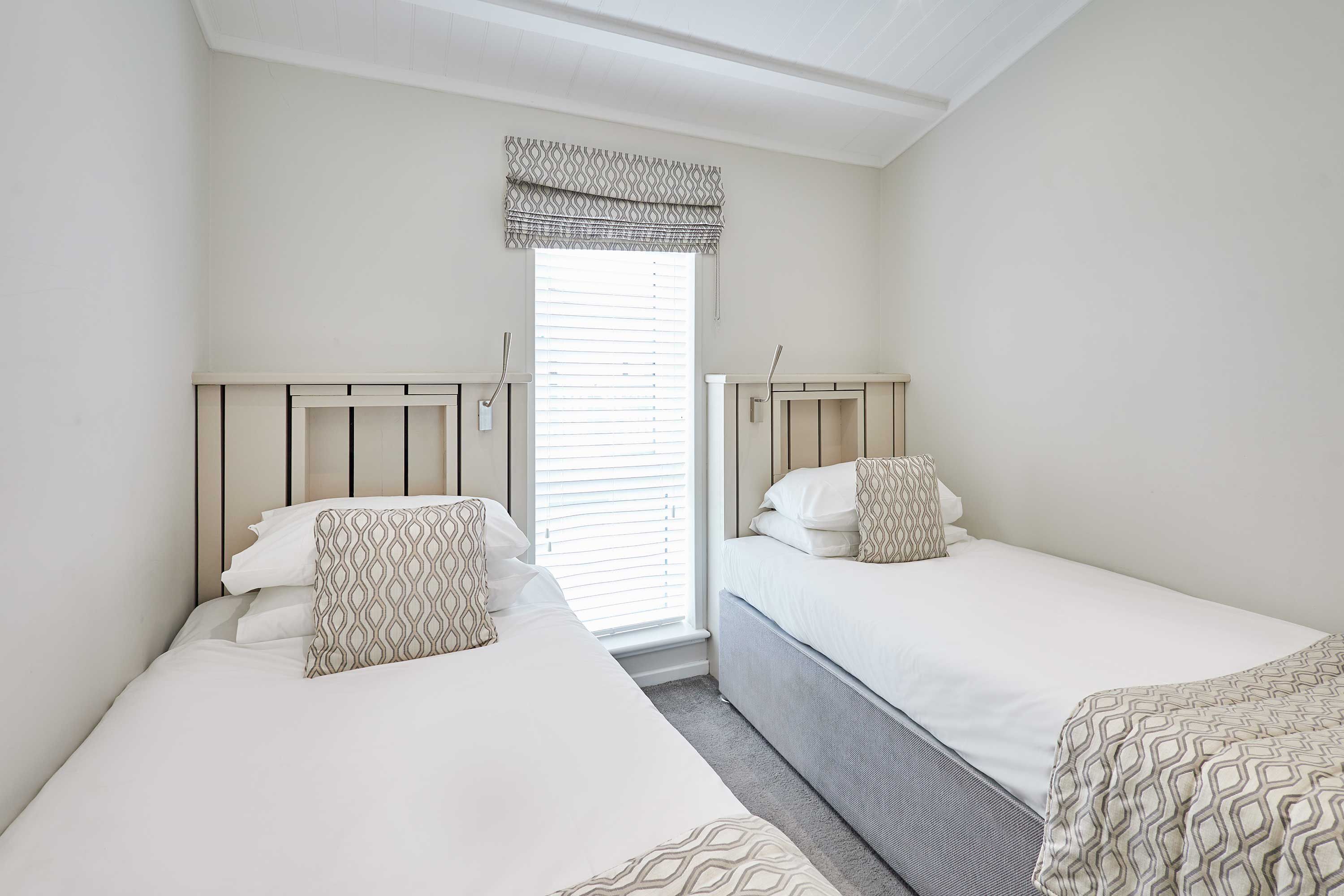A bedroom with two beds, a window with blinds, and a patterned valance.