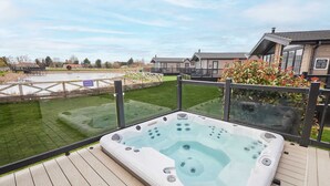 A hot tub on a wooden deck with a view of a lake and buildings in the background. - Host Stay River Tees Lodge (Middlesbrough)