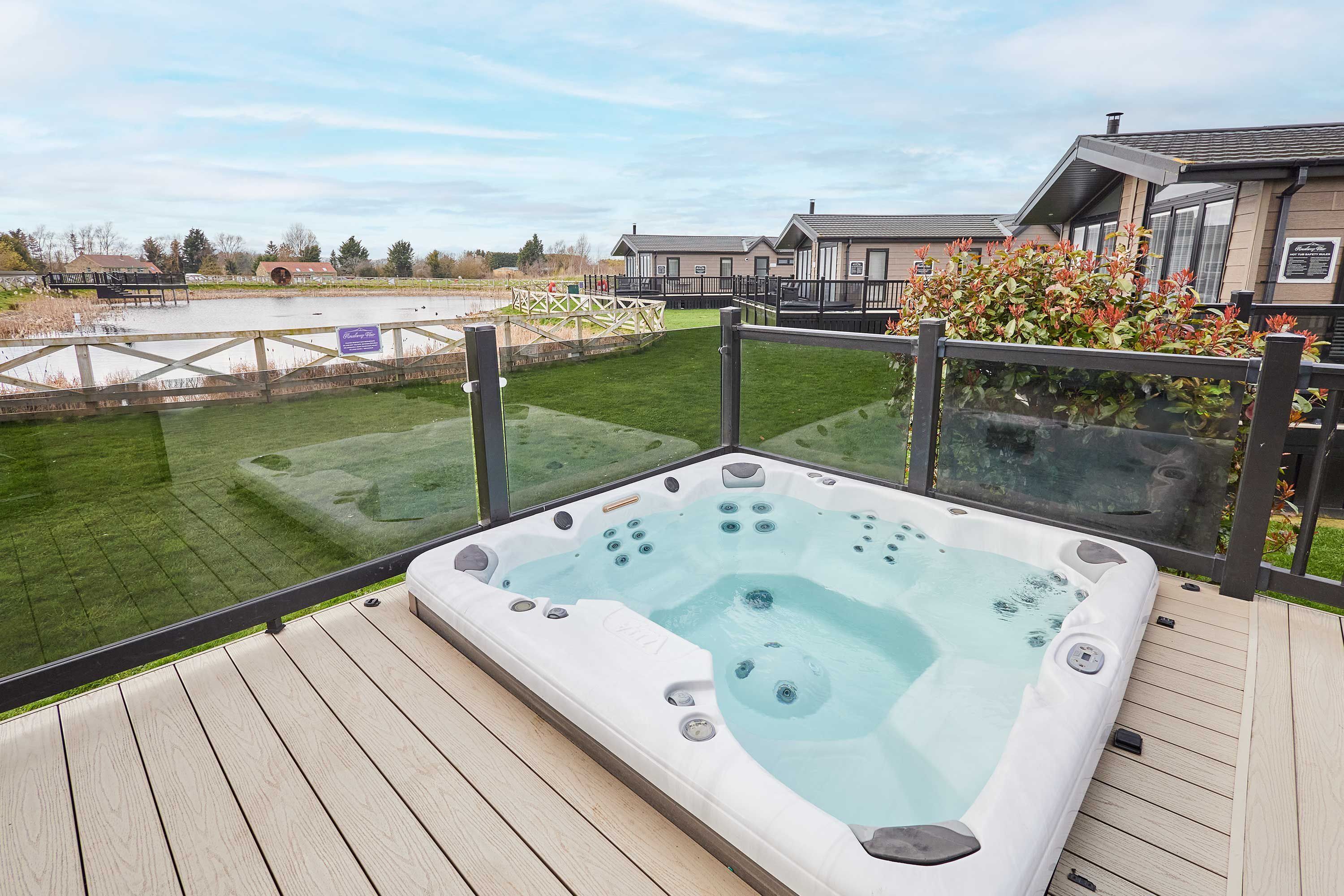 A hot tub on a wooden deck with a view of a lake and buildings in the background.