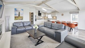A spacious living area with a grey sectional sofa, a dark coffee table, and a dining area with orange chairs. - Host Stay The Riverside Lodge (Middlesbrough)
