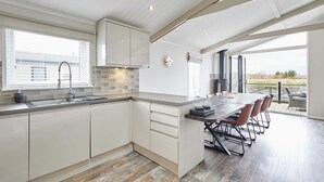 A modern kitchen with white cabinetry, a large island with bar stools, and a view of the outdoors through large windows. - Host Stay The Riverside Lodge (Middlesbrough)