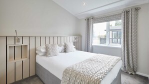 A bedroom with a bed, a headboard, a window with curtains, and a view of the outside. - Host Stay Captain Cook Lodge (Middlesbrough)