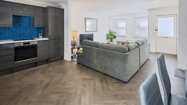 A modern kitchen with grey cabinets, a blue backsplash, and a herringbone-patterned floor. - Host Stay Farm Road (Hove)