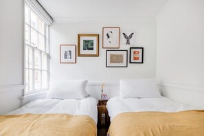 Habitación de hotel con dos camas, una ventana y cuatro obras de arte enmarcadas en la pared.