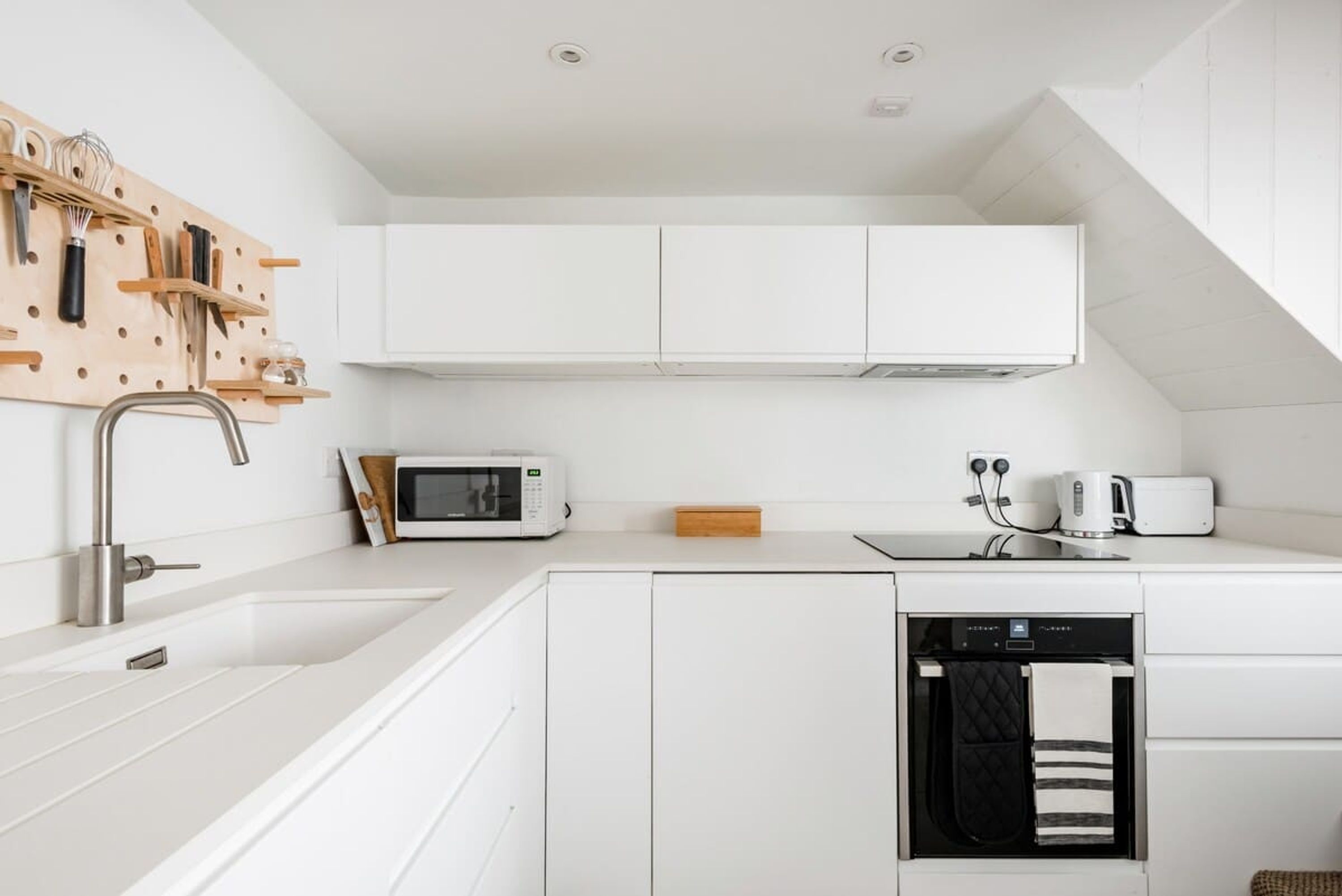 Eine moderne Küche mit weißen Schränken, einer Holz-Dosenwand mit Kochutensilien, einer Mikrowelle, einem Toaster und einem Geschirrspüler.