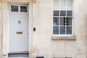 A white door with a brass knocker and a mail slot, a window with multiple panes, and a stone wall.