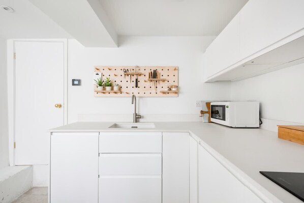 A modern kitchen with a white countertop, a wooden pegboard above the sink, and a microwave on the right. - Central Georgian Townhouse With Free Parking (Bath)