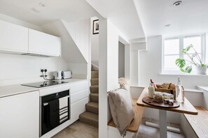 A modern kitchen with white cabinetry, a built-in oven, and a dining area with a wooden table and a plant. - Central Georgian Townhouse With Free Parking (Bath)