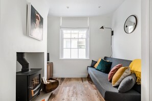 A modern living room with a black wood-burning stove, a grey sofa with colorful cushions, a large window, and a wall-mounted mirror. - Central Georgian Townhouse With Free Parking (Bath)