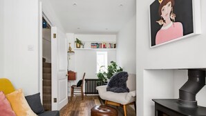 Un salon chaleureux avec un canapé, un pouf et une cheminée. On y trouve une bibliothèque remplie de livres et une plante.