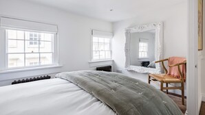 Une chambre à coucher avec un lit, deux fenêtres, un radiateur, un miroir et une chaise.