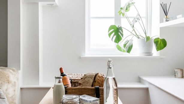 Un coin accueillant avec une table en bois sur laquelle se trouvent une bouteille, un bocal en verre et un panier en osier.
