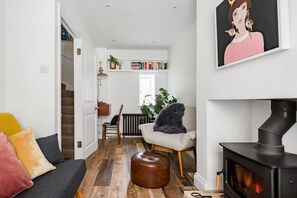 A cozy living room with a sofa, ottoman, and a fireplace. There is a bookshelf with books and a plant. - Central Georgian Townhouse With Free Parking (Bath)