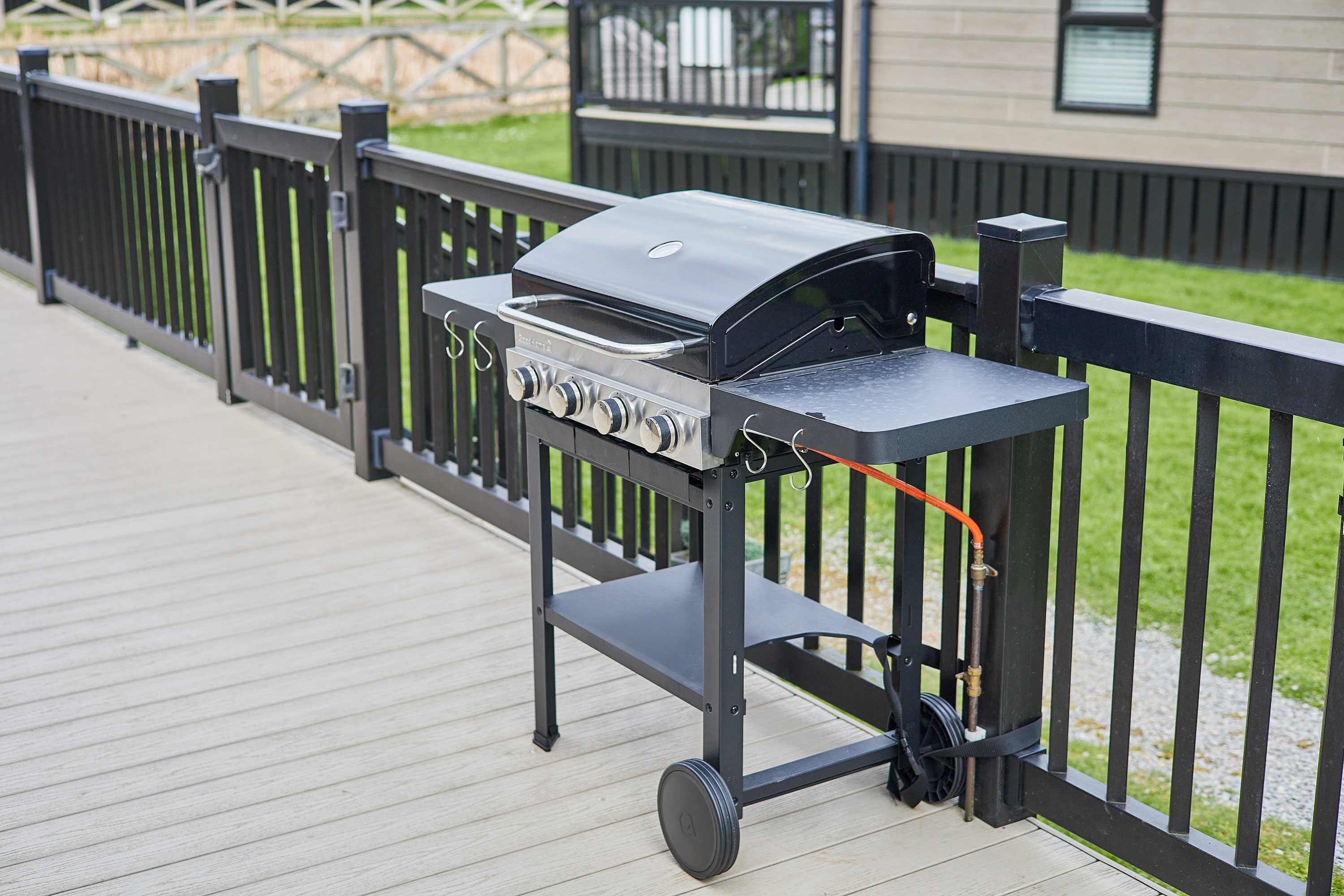 Een draagbare barbecue op een houten terras met een zwarte metalen reling.